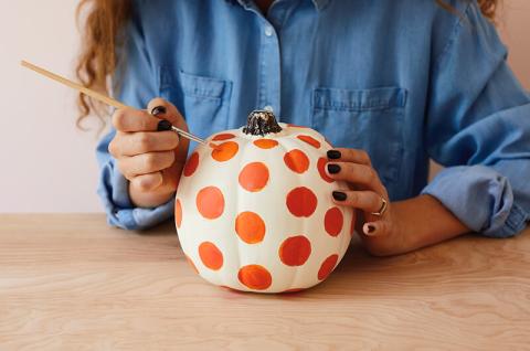 A woman holding a paintbrush is painting a polka dot pumpkin